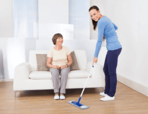caretaker cleaning the floor with a mop while a senior woman sitting on the sofa